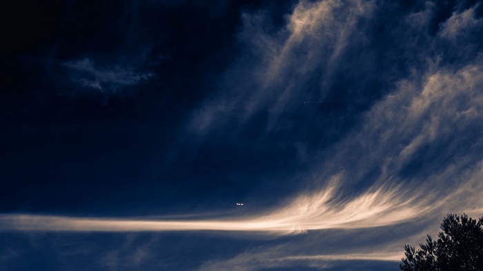 Airplane flying through dramatic clouds at dusk