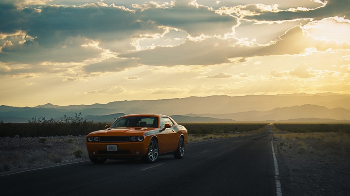 Orange Dodge Challenger on a desert road at sunset