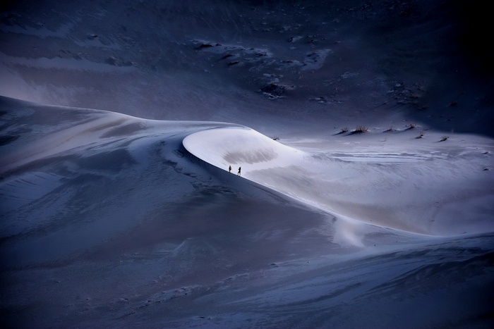 Two people walk on a sand dune in the desert