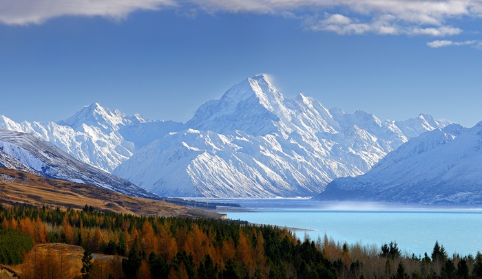 Snow-capped mountains overlooking a turquoise lake and autumn forest