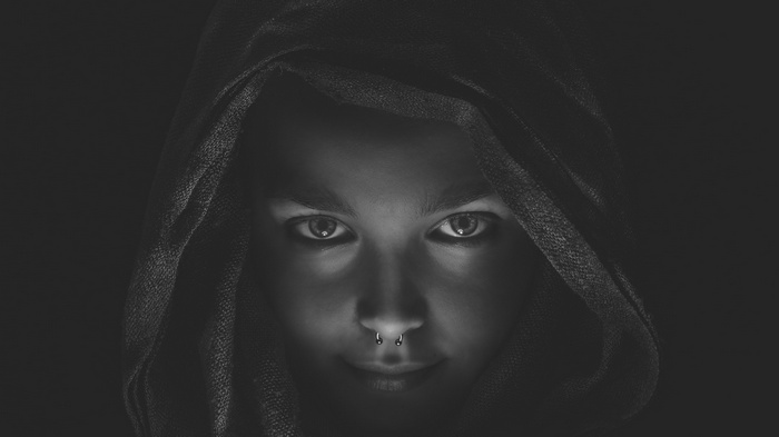 Monochrome portrait of a person with a pierced nose wearing a hood