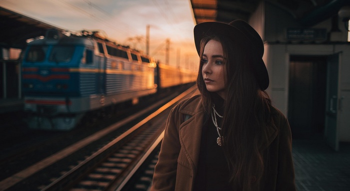 Woman in hat on train platform at sunset