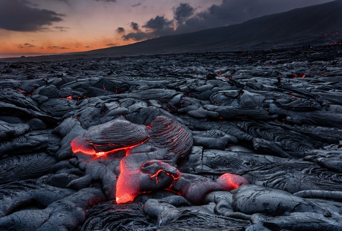 Molten lava flows over a rocky landscape at sunset