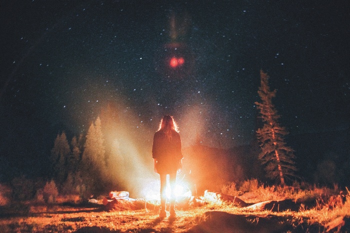 Woman standing by campfire under starry night sky