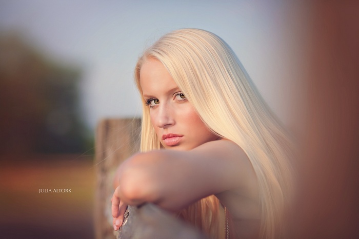 Woman with blonde hair leaning on a wooden fence
