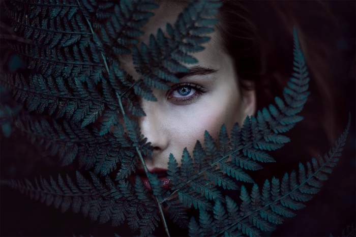 Woman with blue eyes peeking through fern leaves