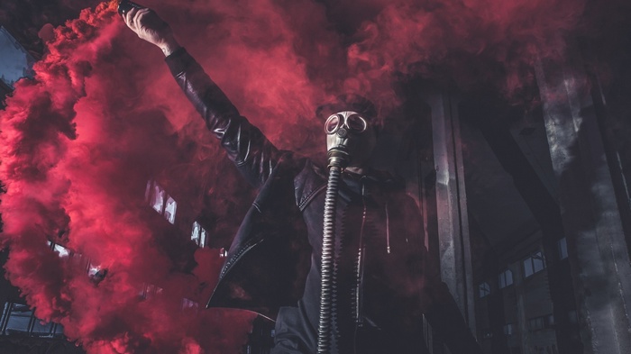 Person in gas mask holding red smoke bomb