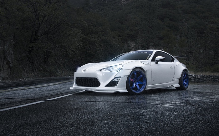 White Scion FR-S with blue wheels on a wet road
