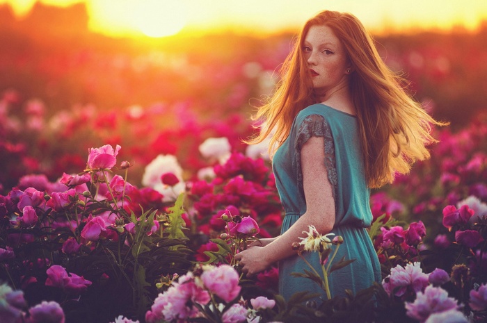 Redhead woman in a field of peonies at sunset
