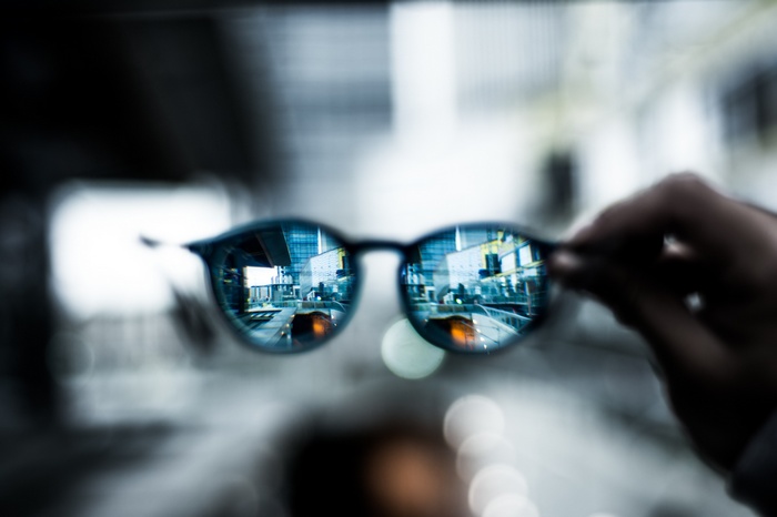 City reflected in sunglasses held by a hand