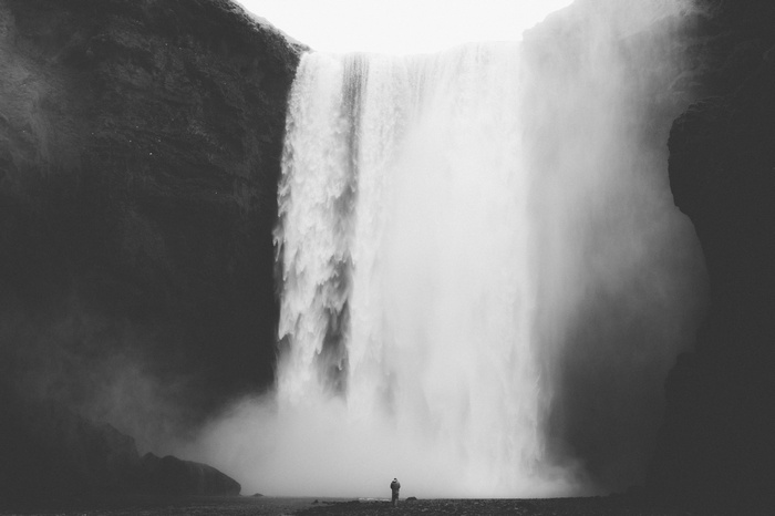 A lone person stands before a massive waterfall