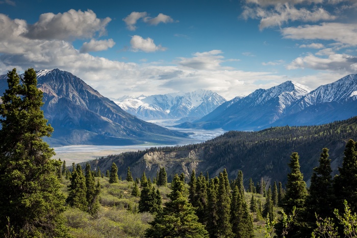 Mountain range with river and trees under cloudy sky