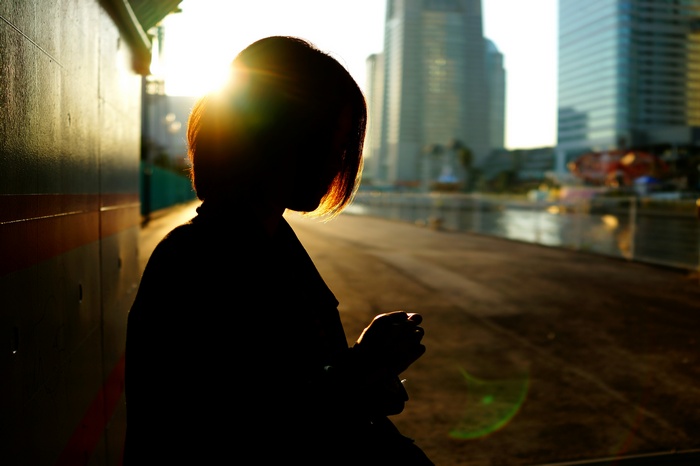 Silhouette of an Asian woman against city buildings at sunset