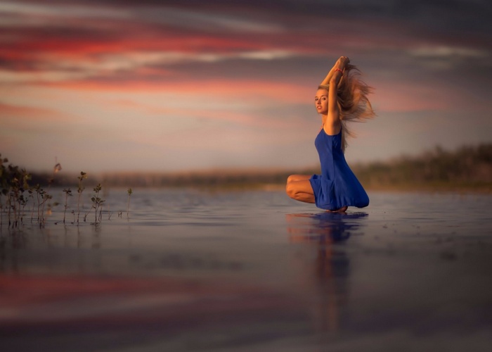 Woman in blue dress posing in water at sunset