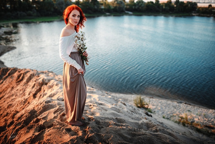 Redhead woman with flowers by the lake at sunset