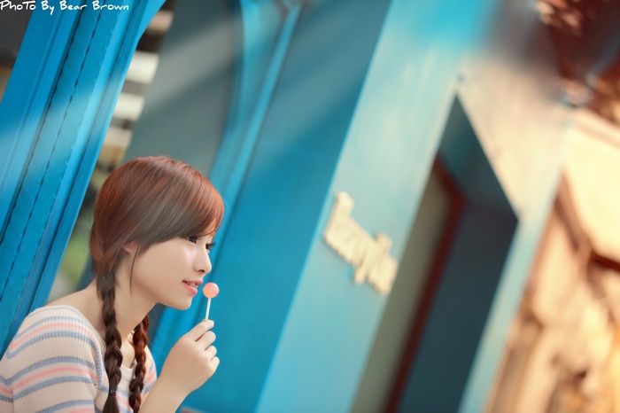 Asian woman with auburn hair eating a lollipop