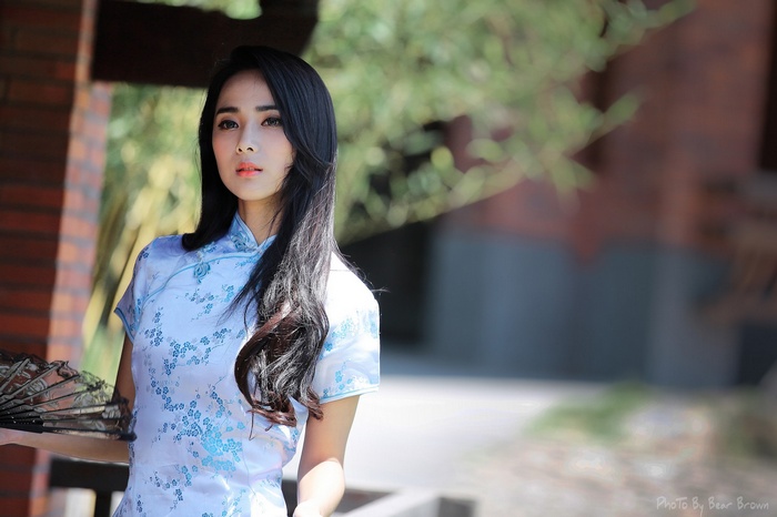 Woman in a traditional blue floral dress holding a fan