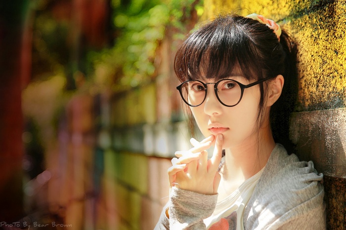 Asian girl with glasses leaning against a wall