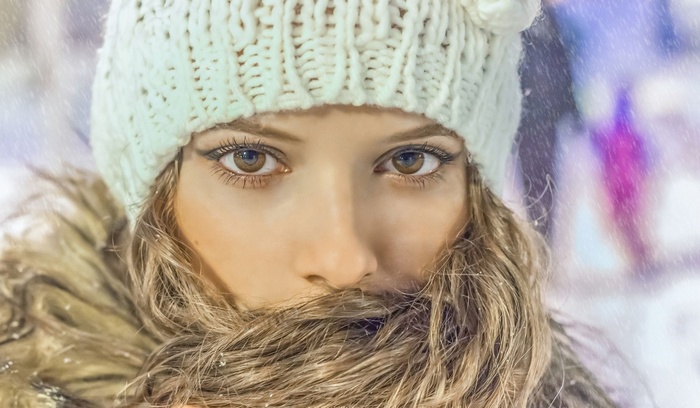 Woman in a white knitted hat and fur collar in the snow