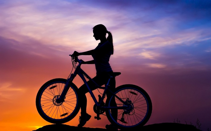 Silhouette of a woman with a bicycle at sunset