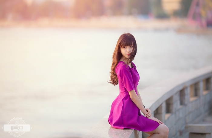 Asian woman in purple dress sitting by the water