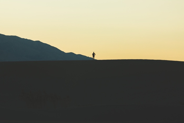 Silhouette of a person on a sand dune with mountains