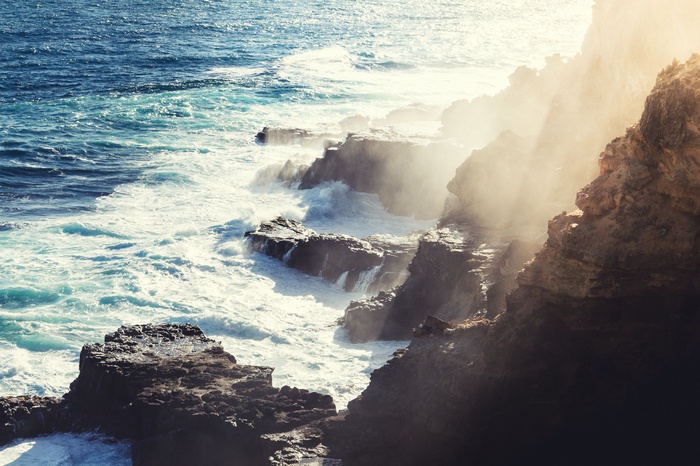 Waves crashing on rocky cliffs with sunlight