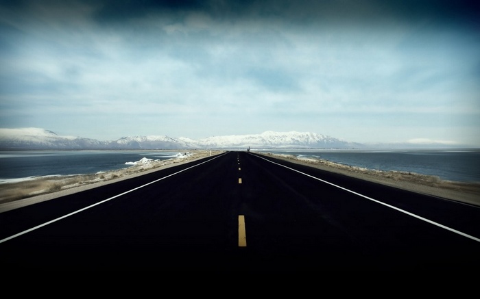 A long, empty road stretches towards snow-capped mountains.