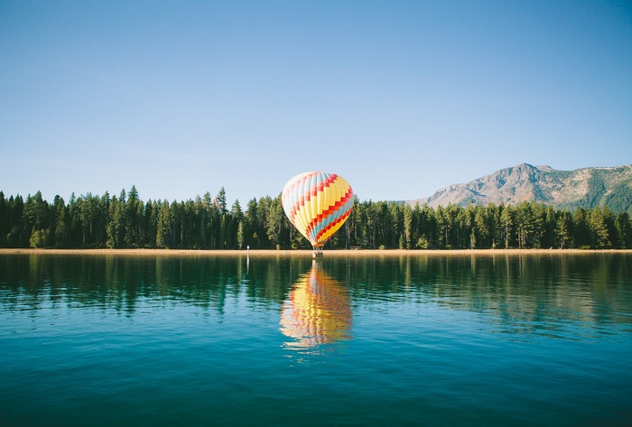 Hot air balloon over a lake with forest and mountains
