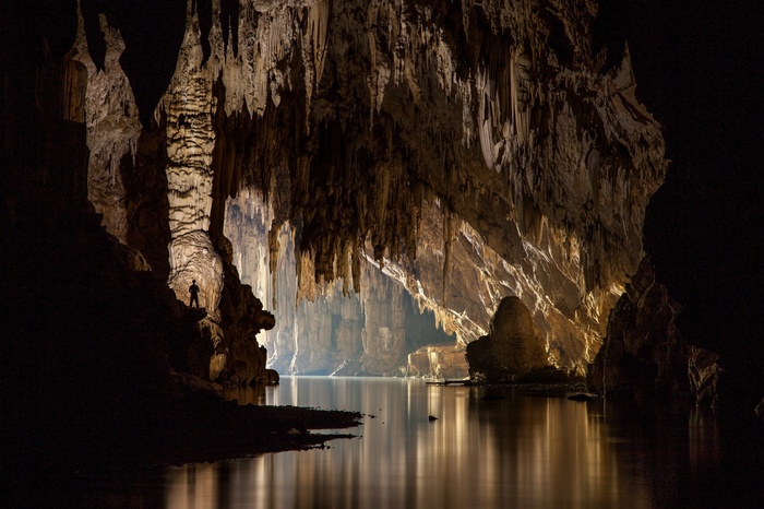 Man standing in a vast cave with a body of water