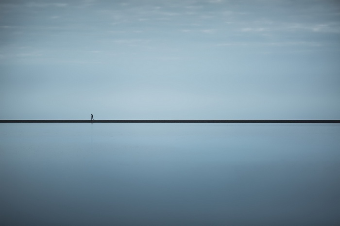 A lone figure walks on a thin line across water