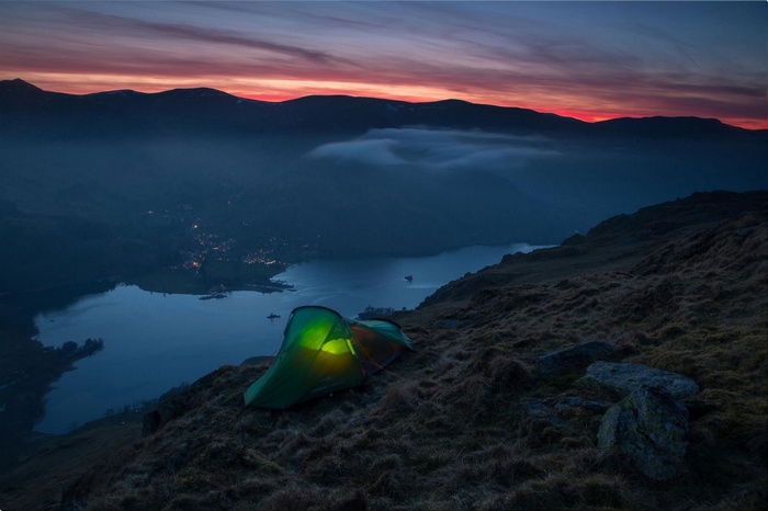 Tent on a mountain overlooking a lake at sunset