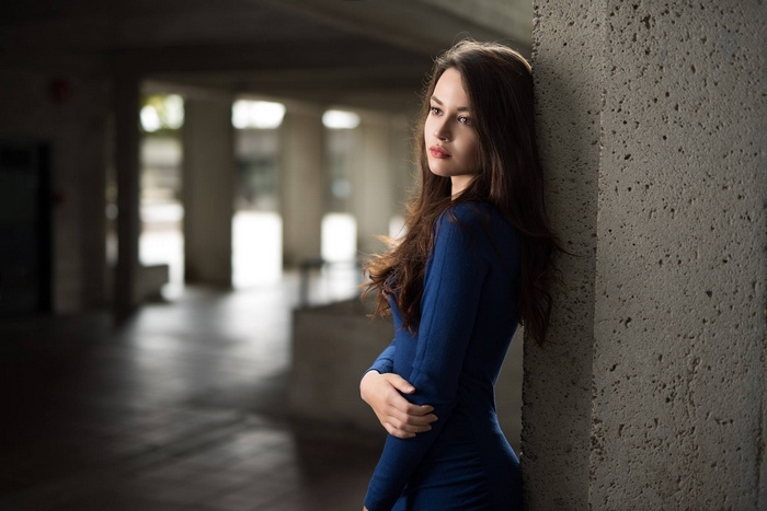 Woman in blue dress leaning against concrete pillar