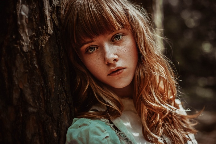 Portrait of a young girl with freckles leaning against a tree