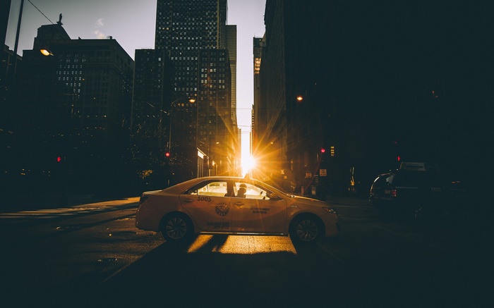 Yellow taxi driving down a city street at sunset