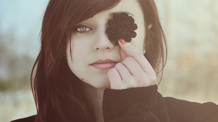 Woman holding a black flower over her eye