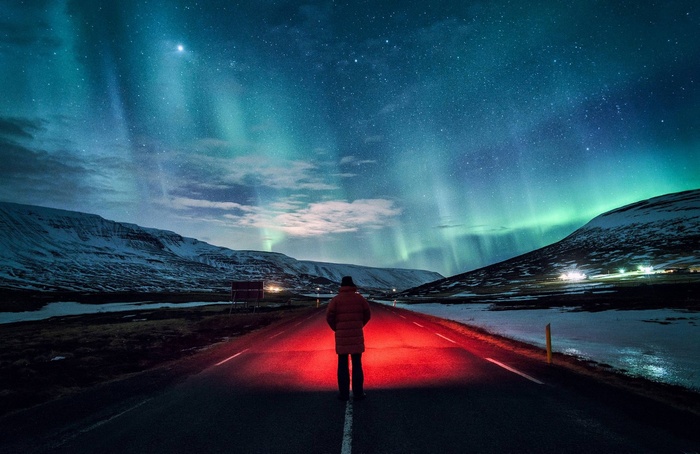 Person standing on road under aurora borealis