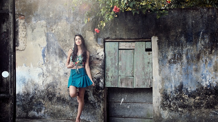 Woman in skirt leaning against a weathered wall