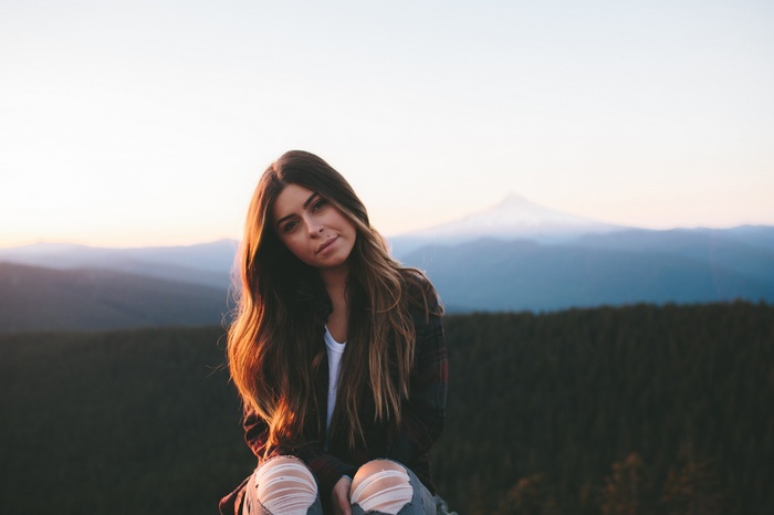 Woman with long hair sitting outdoors with mountains in background