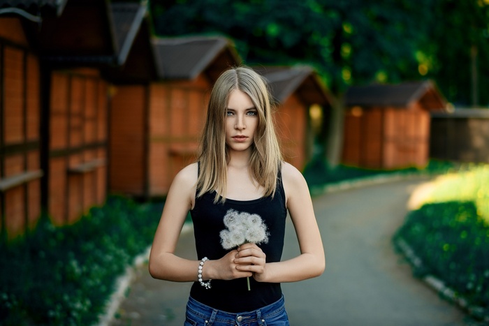 Woman holding dandelions in front of wooden huts