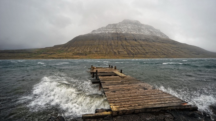 Old wooden pier on a stormy sea with mountains