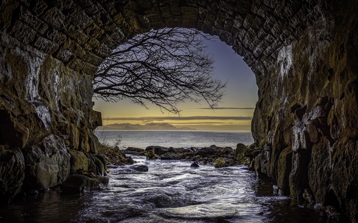 Stone tunnel framing a view of the sea and mountains
