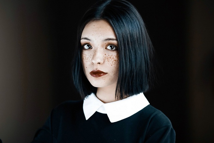 Woman with black hair and freckles wearing black clothing