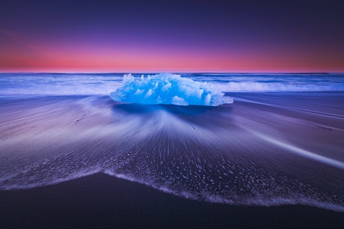 Blue iceberg on a black sand beach at sunset in Iceland