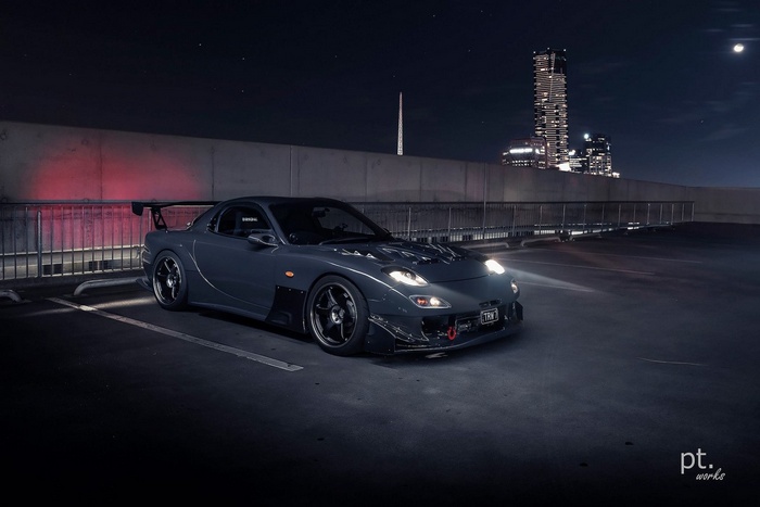 Tuned Mazda RX-7 parked at night with city skyline