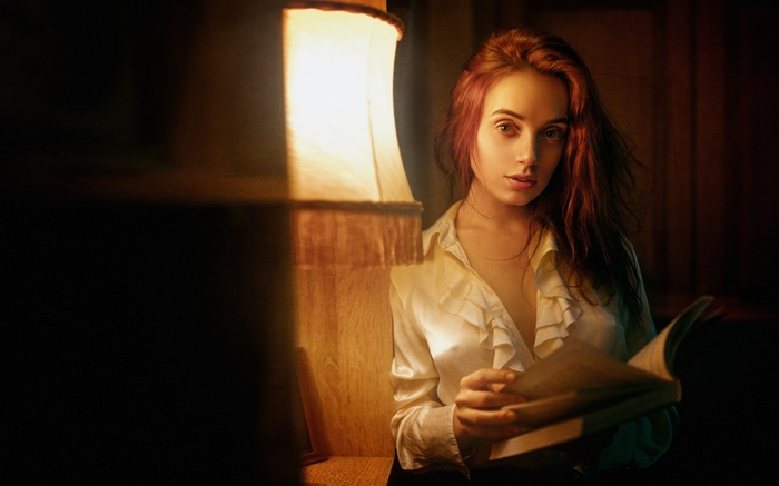 Woman reading a book by a lamp