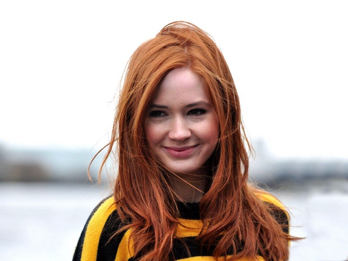 Karen Gillan smiling in a yellow and black striped sweater