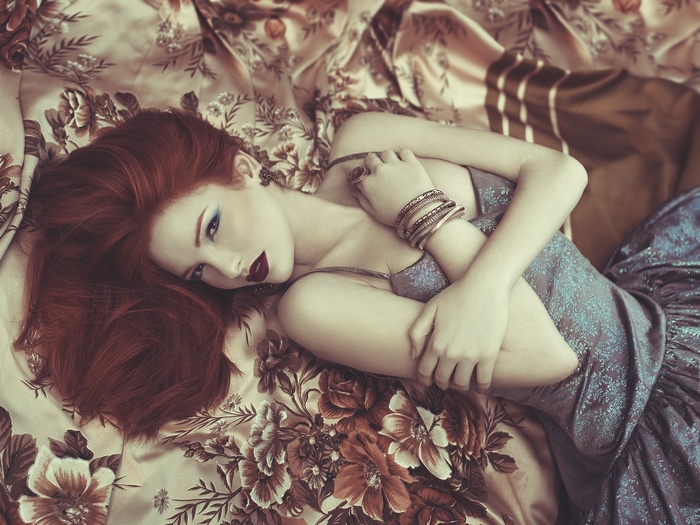 Redhead woman with red lipstick and bangles lying on floral fabric