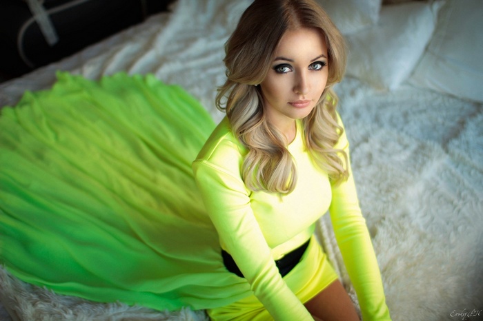 Woman with blonde curly hair in a yellow dress on a bed