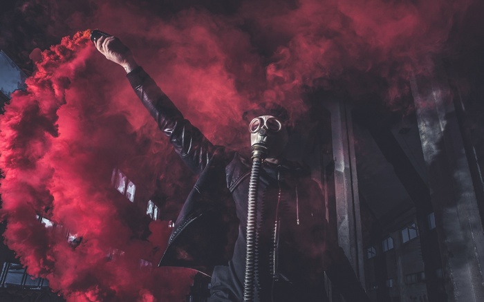 Man in gas mask holding red smoke bomb